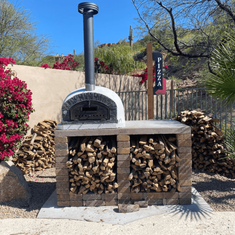 Outdoor pizza oven on a wood-stacked base with a "PIZZA" sign nearby